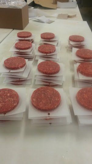 Several stacks of raw hamburger patties, each separated by parchment paper, are arranged on a white table.