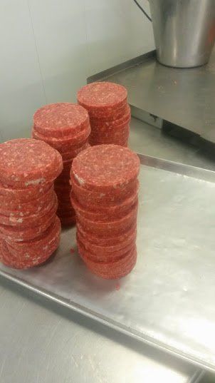 Four stacks of raw, circular ground meat patties arranged on a metal tray in a kitchen.