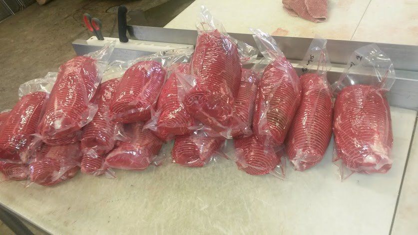 Multiple vacuum-sealed packages of raw, red meat resting on a white surface in a commercial kitchen setting.