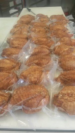 A row of vacuum-sealed, roasted golden-brown chicken halves arranged on a clean white surface.