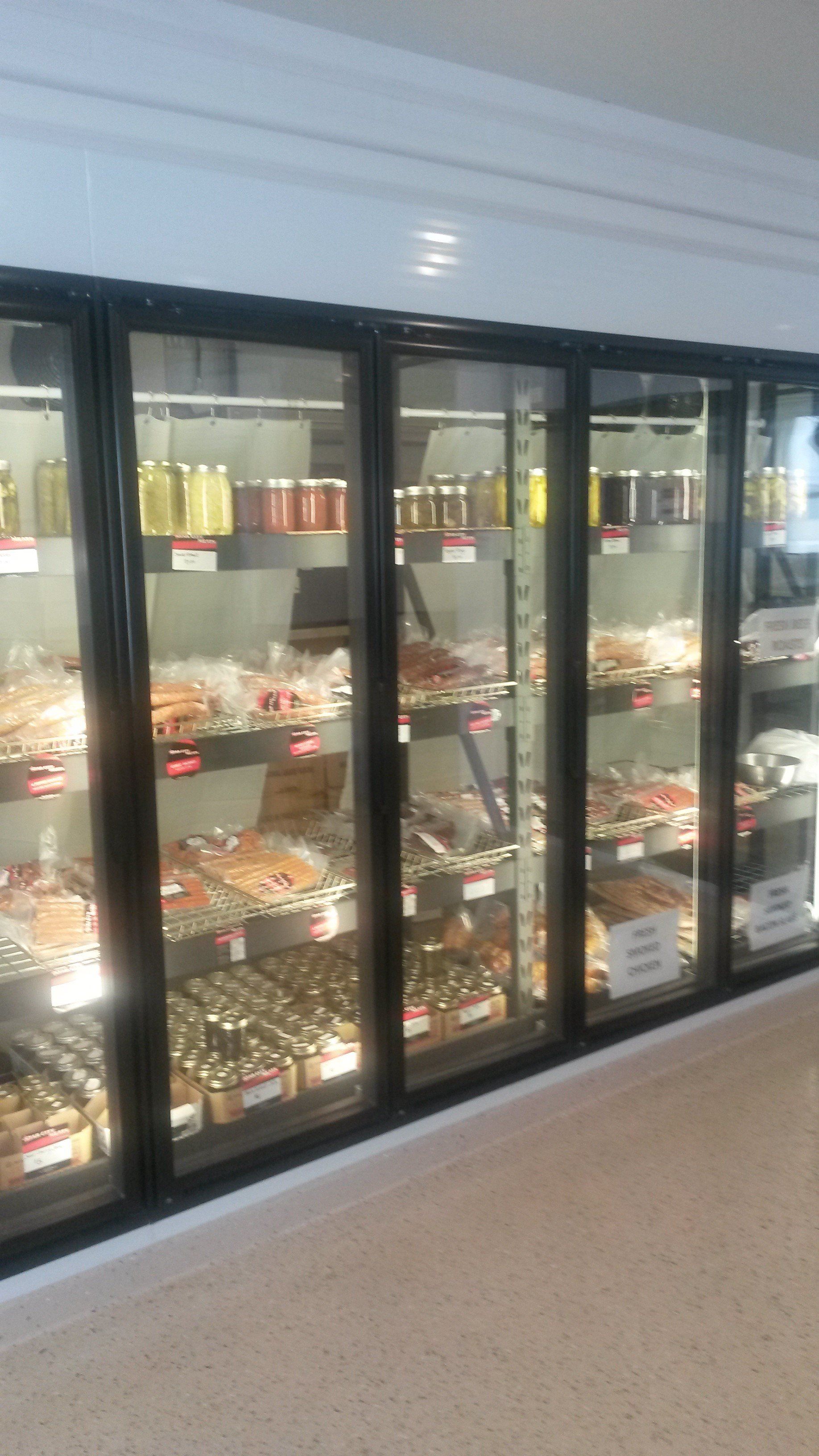 A row of refrigerated display cases in a store filled with various jars of food, packaged meats, and other grocery items.