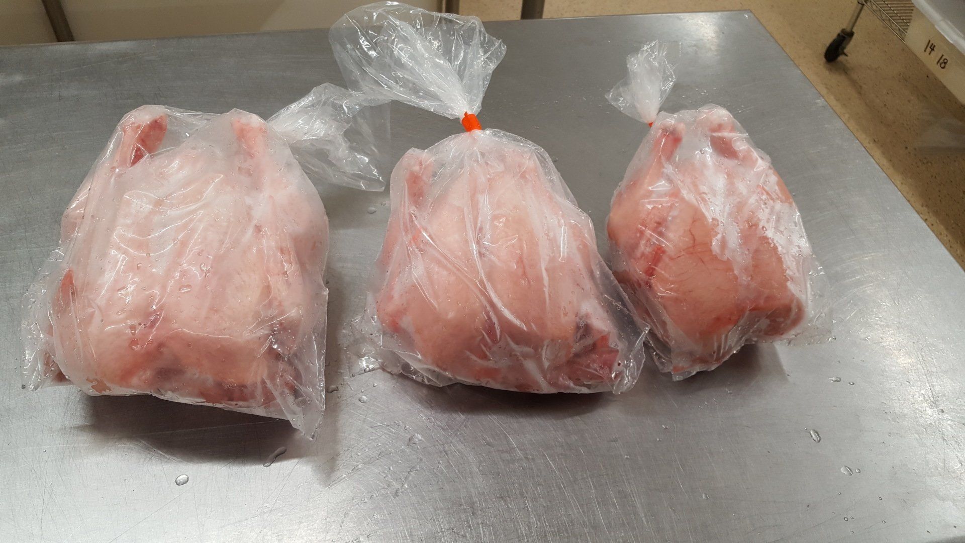 Three raw, whole chickens individually wrapped in clear plastic bags, sitting on a stainless steel surface.