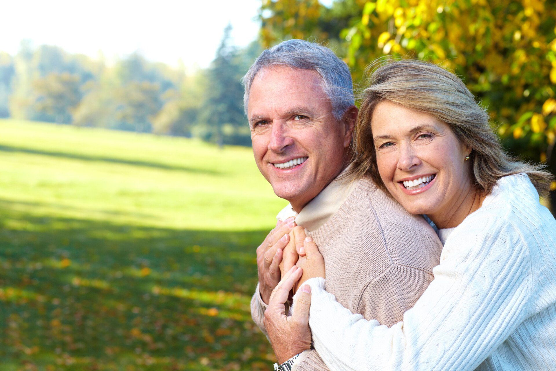 A man and a woman are hugging each other in a park.
