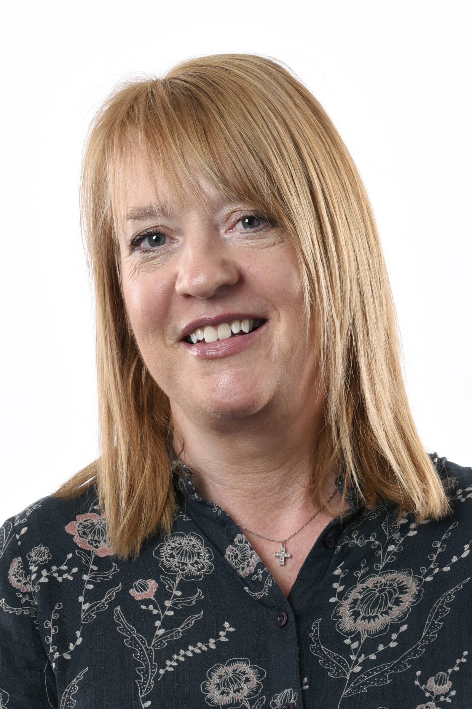 A woman with blonde hair is smiling and wearing a floral shirt.
