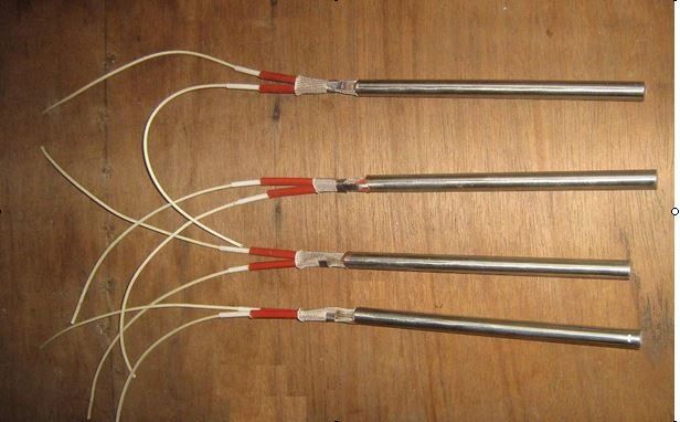 Cuatro sondas metálicas en forma de varilla con cables blancos y conectores rojos dispuestas sobre una superficie de madera.