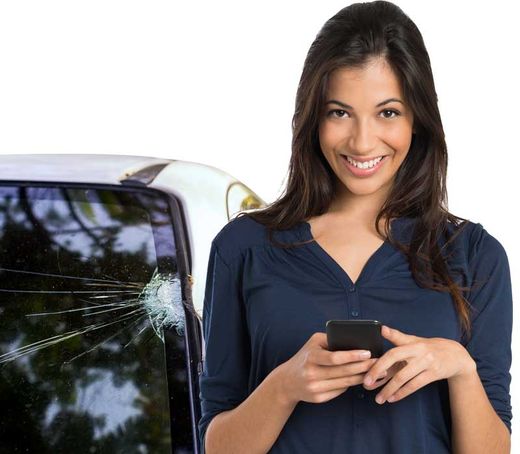 Une femme sourit, tenant un téléphone près d'une voiture au pare-brise fissuré.