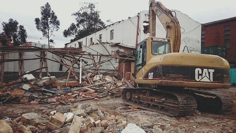Una excavadora CAT demuele un edificio derrumbado entre escombros y restos.