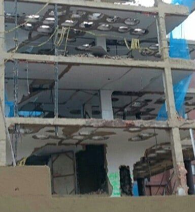 Edificio de varias plantas dañado con vigas expuestas, paredes rotas y escombros colgantes tras el derrumbe estructural.