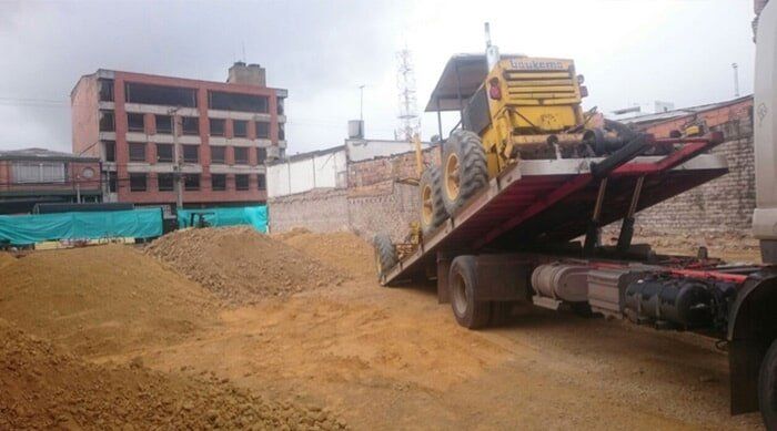 Obra en construcción con un camión volquete descargando arena junto a un edificio en construcción.