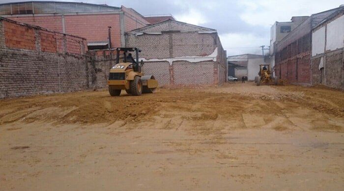 Obra en construcción con un rodillo amarillo compactando la tierra entre edificios de ladrillo.