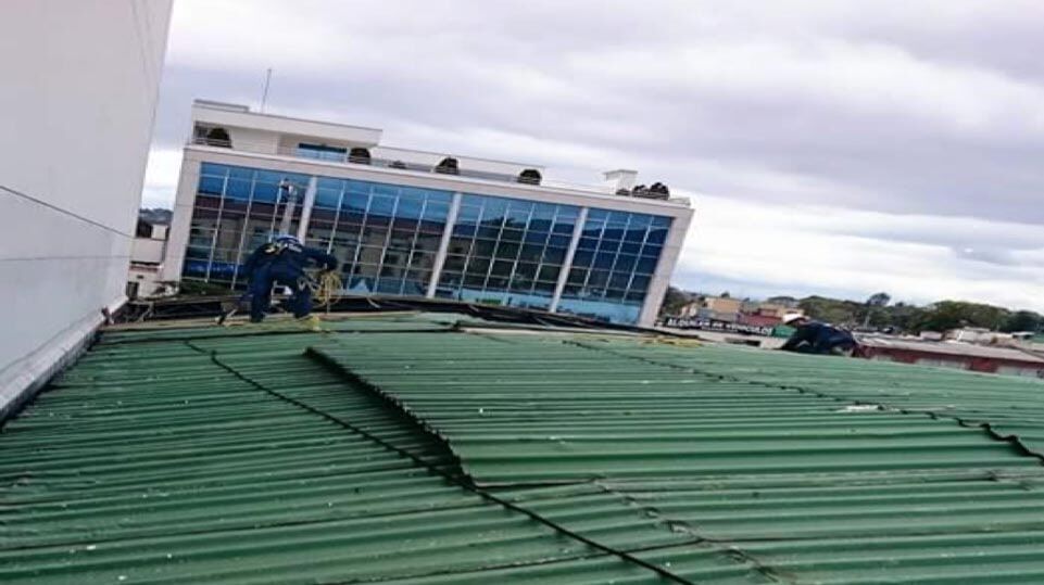 Vista inclinada de un tejado metálico verde con un edificio de cristal azul al fondo, bajo un cielo nublado.