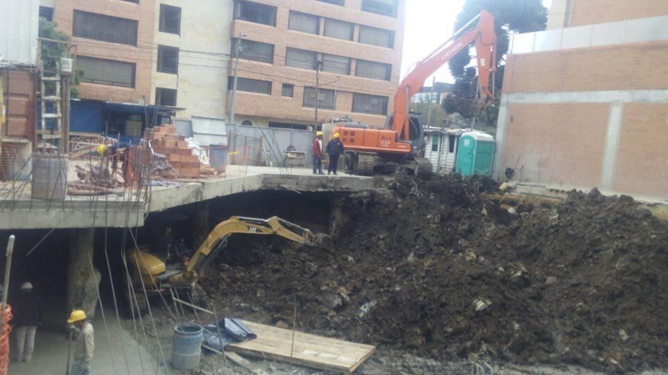 Excavadora y zona de construcción junto a una excavación derrumbada bajo un edificio de apartamentos.
