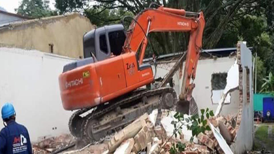 Una excavadora naranja demuele un muro blanco en una obra en construcción