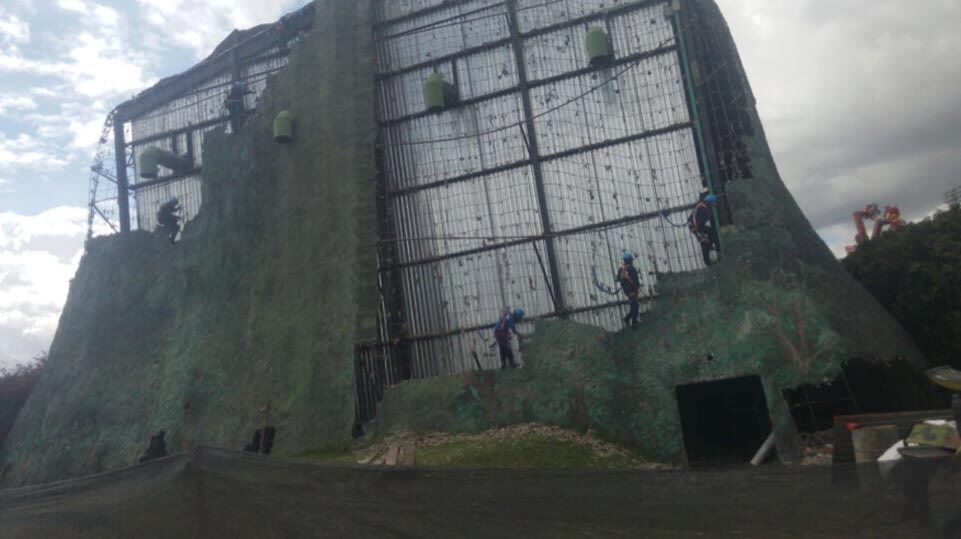 Gran muro de escalada al aire libre con red y cielo nublado.