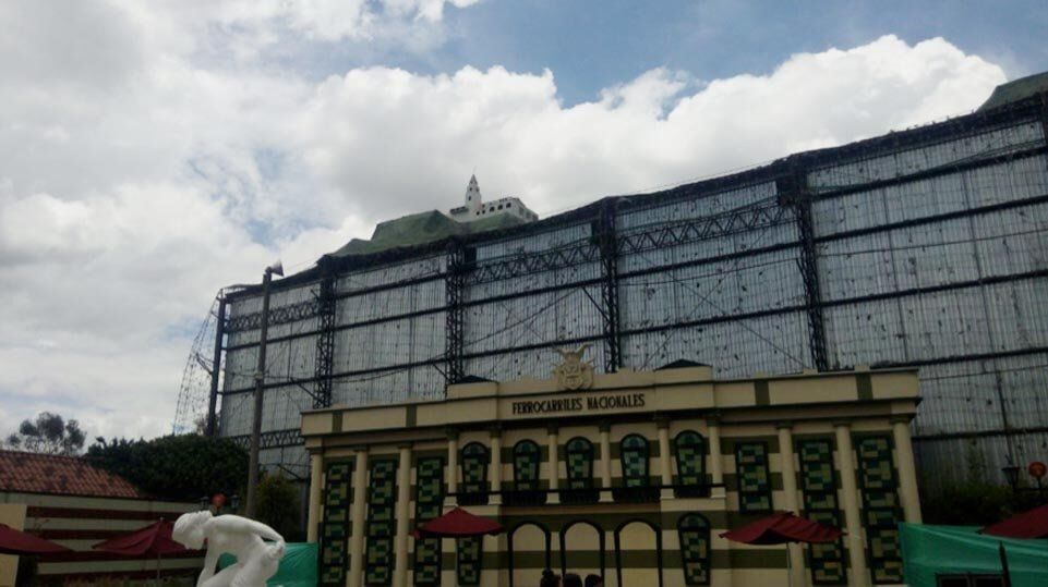 Un gran edificio blanco con marco oscuro detrás de una puerta decorativa amarilla y verde bajo un cielo nublado.