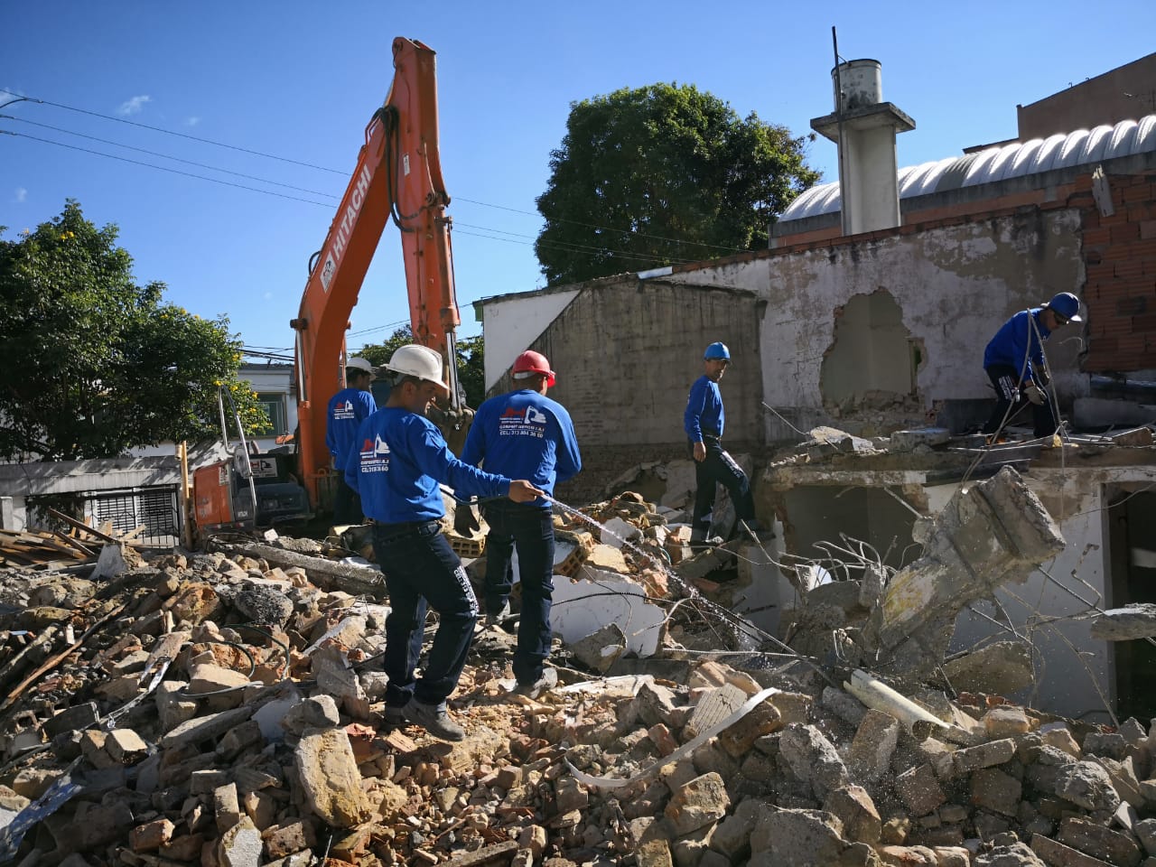 Trabajadores retiran escombros con una excavadora junto a un edificio dañado tras su demolición o derrumbe.