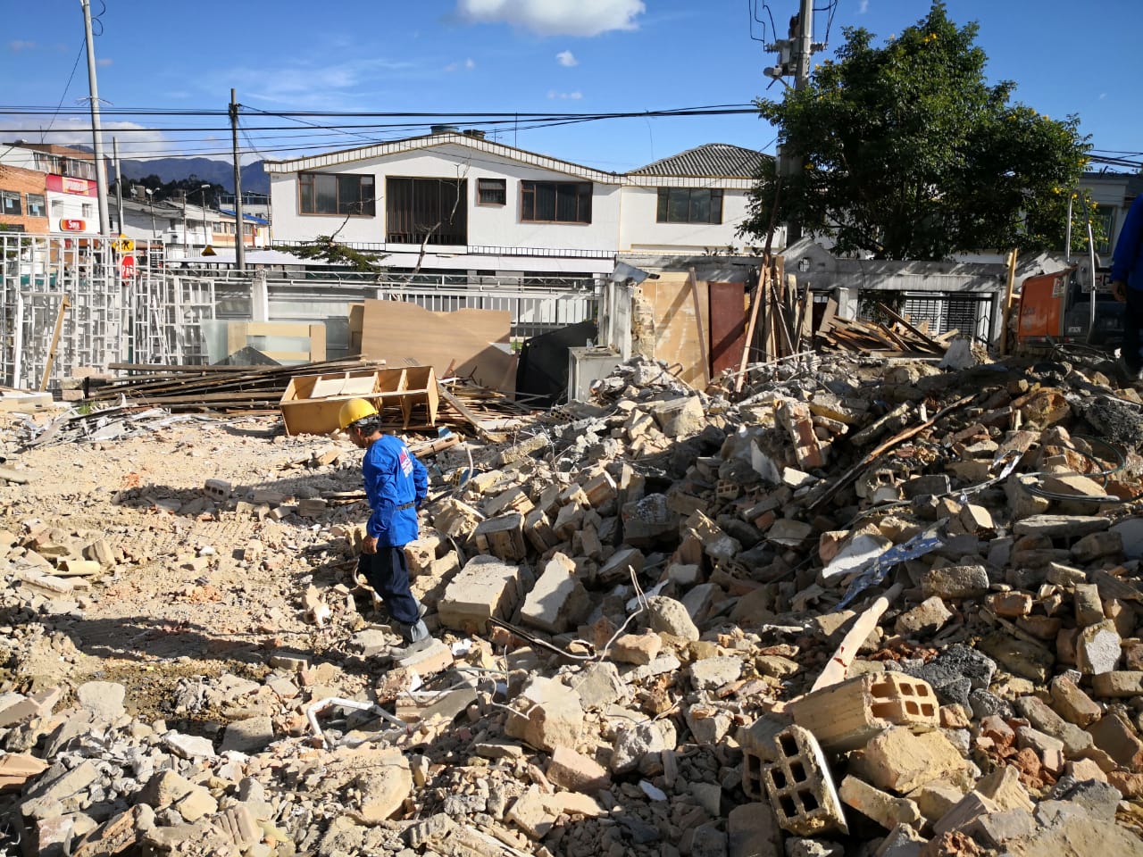 Escombros de demolición frente a una casa blanca; un trabajador vestido de azul se encuentra entre los escombros.
