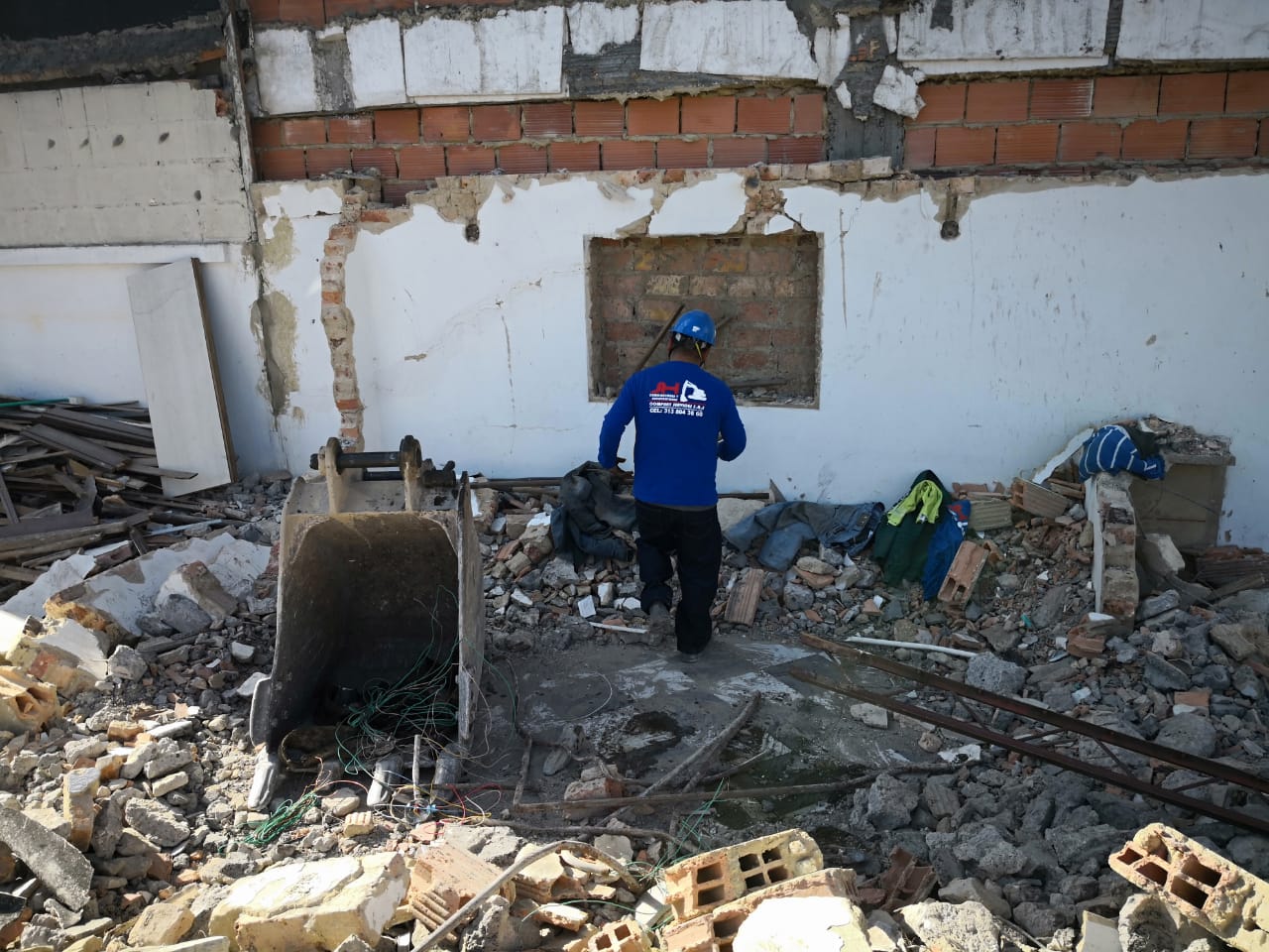 Una persona con chaqueta azul inspecciona los escombros dentro del interior de un edificio dañado.
