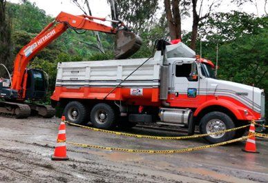 Excavadora naranja cargando tierra en un camión volquete blanco en una obra de construcción embarrada.