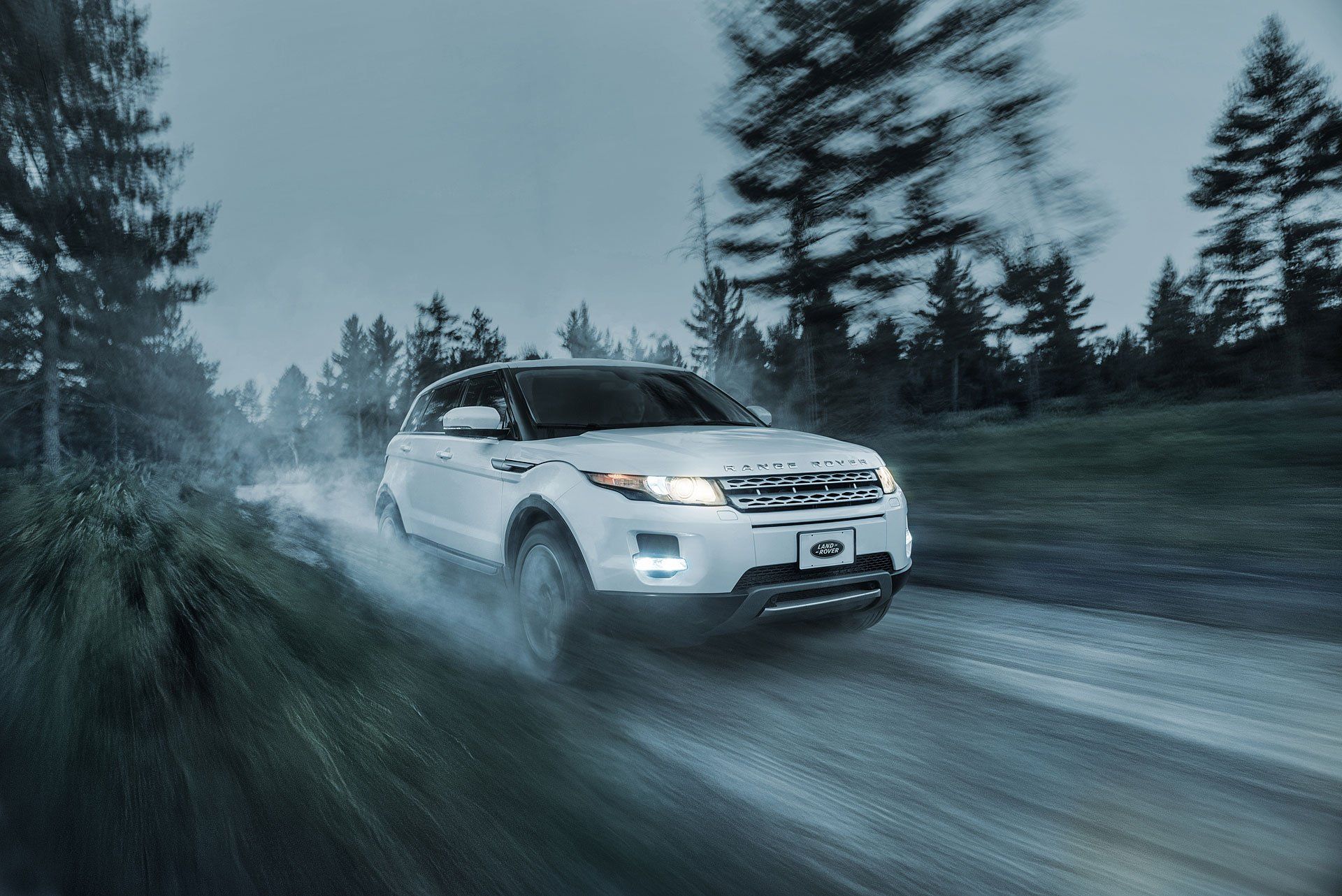 a white range rover evoque is driving down a snowy road .
