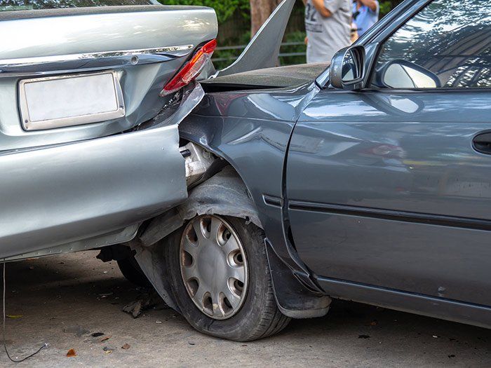 Two gray cars damaged in a rear-end collision; one car's front tire is flat.