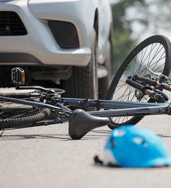 A bicycle lies on the road in front of a silver car; a blue helmet rests nearby, suggesting an accident.