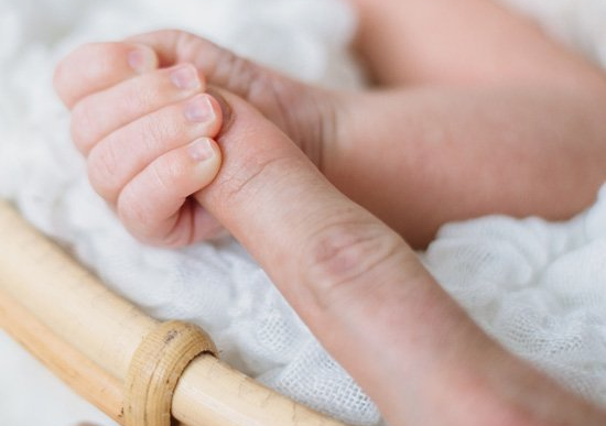 A close-up of a baby's hand grasping an adult finger, resting on a white blanket.