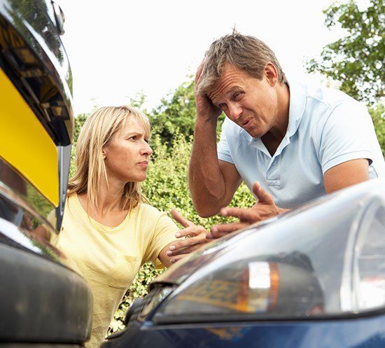 Woman and man examining car damage after a collision; both appear distressed, with one touching their head.