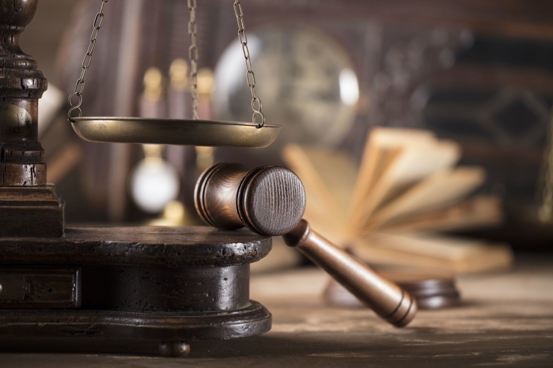 Gavel and scales of justice on a wooden stand, with an open book and clock in the background.