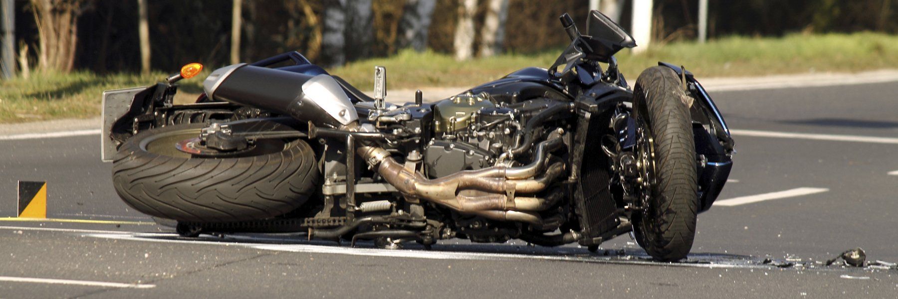 A motorcycle lies on its side on a road, apparently after a crash. The bike is black with exposed engine components.