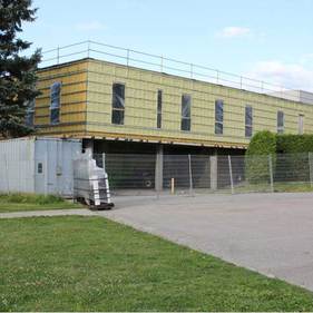 Bâtiment industriel jaune avec fenêtres grillagées, porte sectionnelle et remorque devant, sous un ciel dégagé