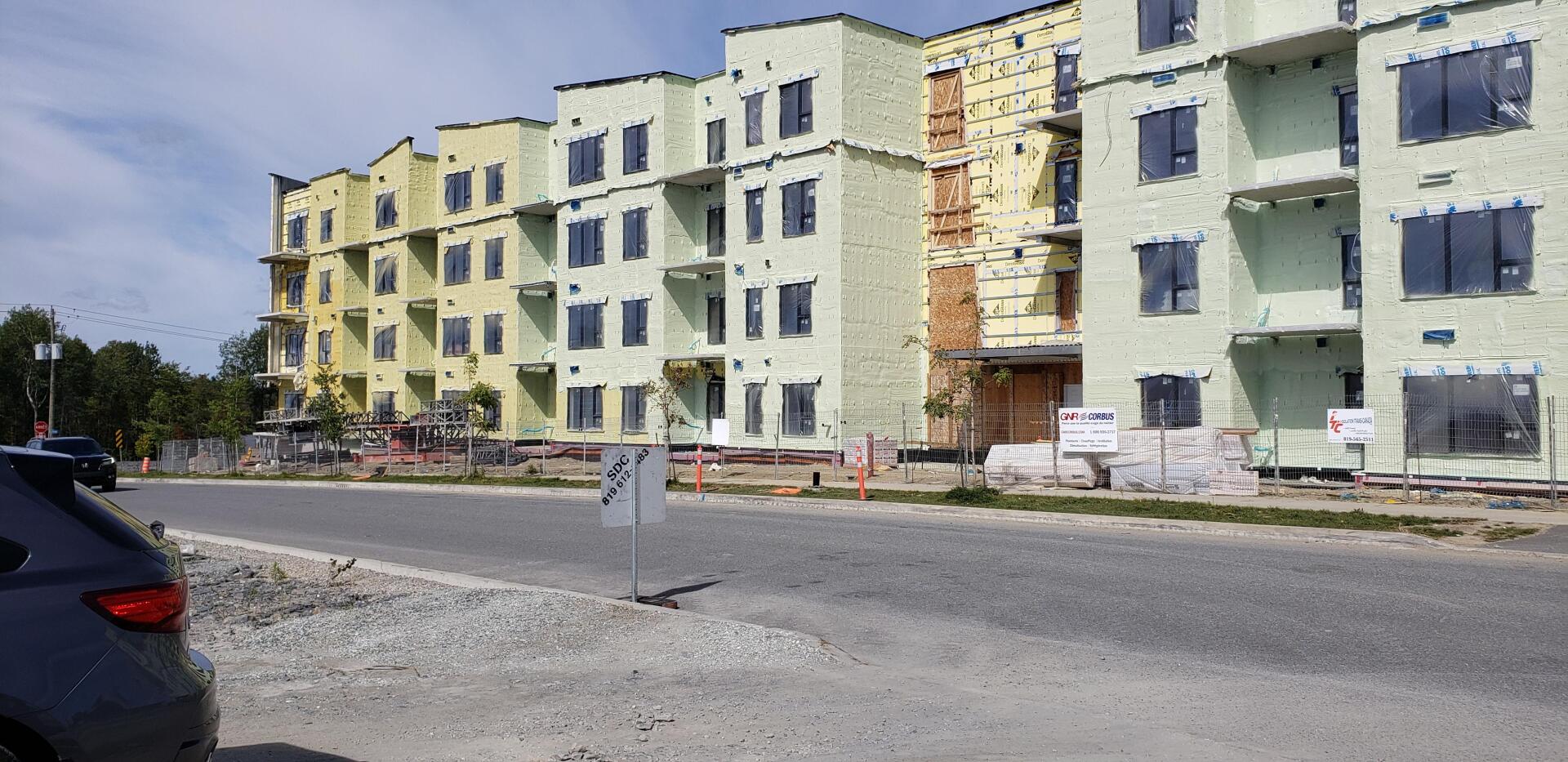 Immeubles d'appartements partiellement démolis, intérieurs apparents, en bordure d'une route et d'une voiture garée.