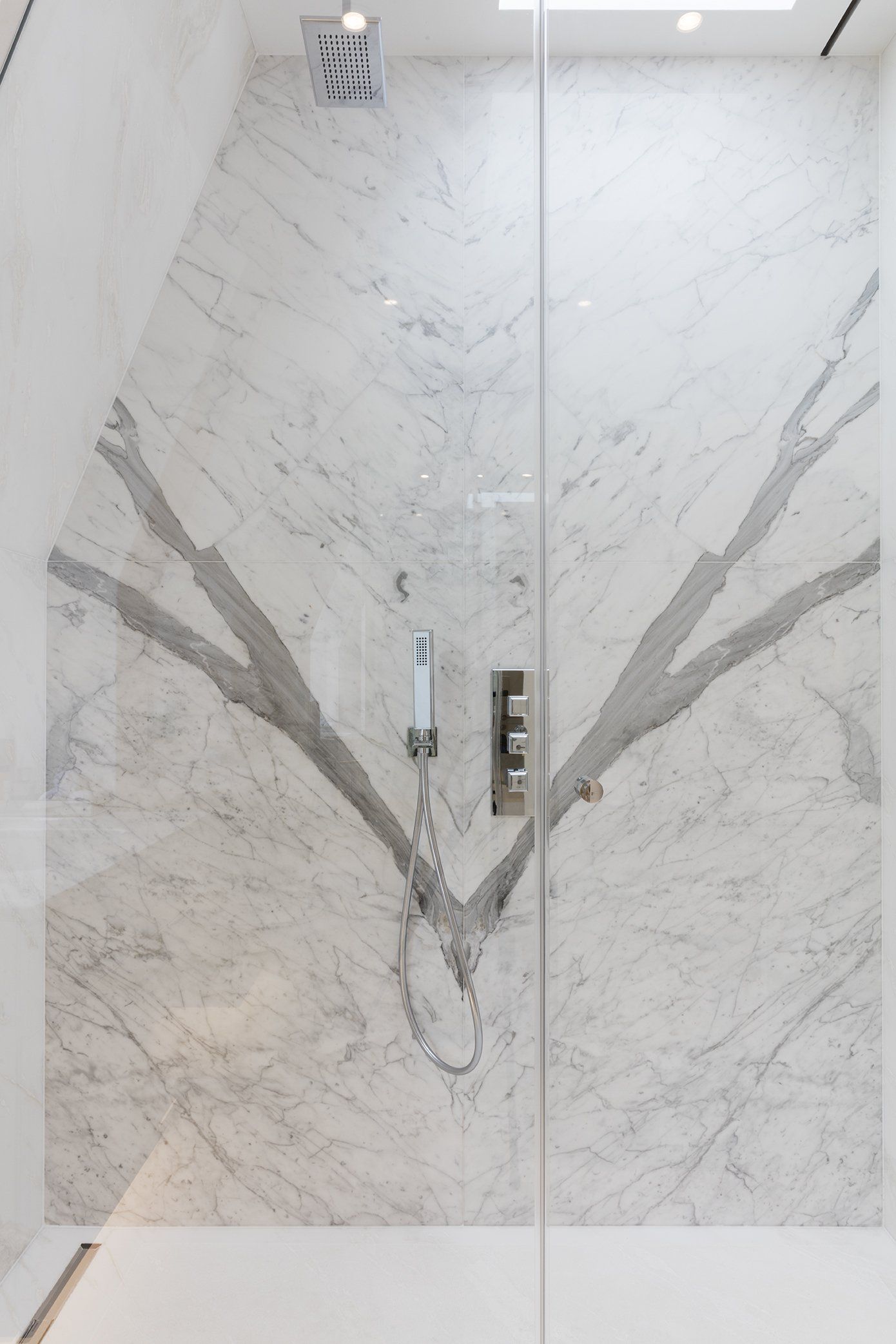 A shower stall with a marble wall and a glass door.