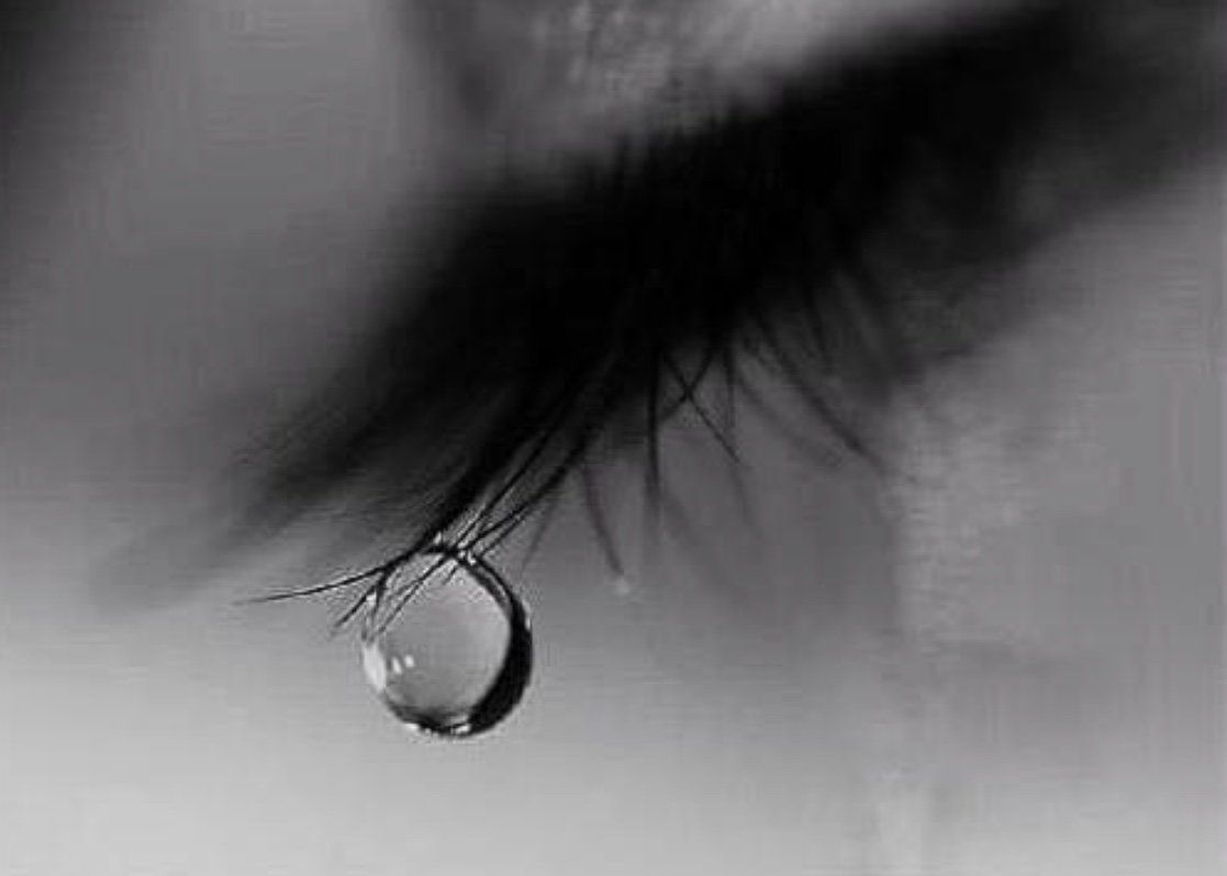 Close-up of an eye, a single tear falling from the lower lashes. Black and white.