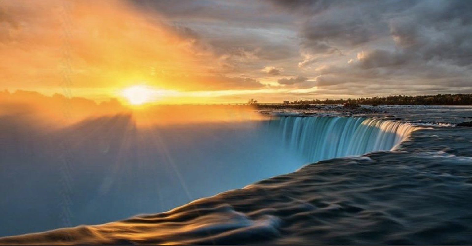Niagara Falls at sunset, with golden sunlight and mist rising from the falls.