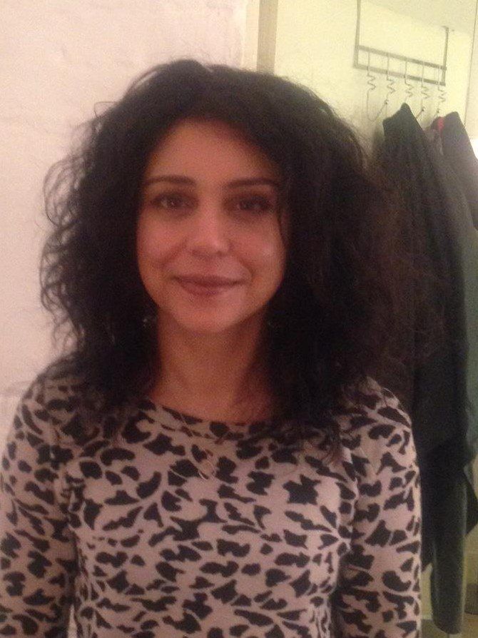 Photo of a smiling woman with a wavy, shoulder-length, dark brown hair wig