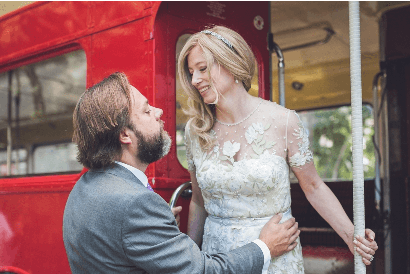 Photo of a bride and groom standing in the entrance to a red bus