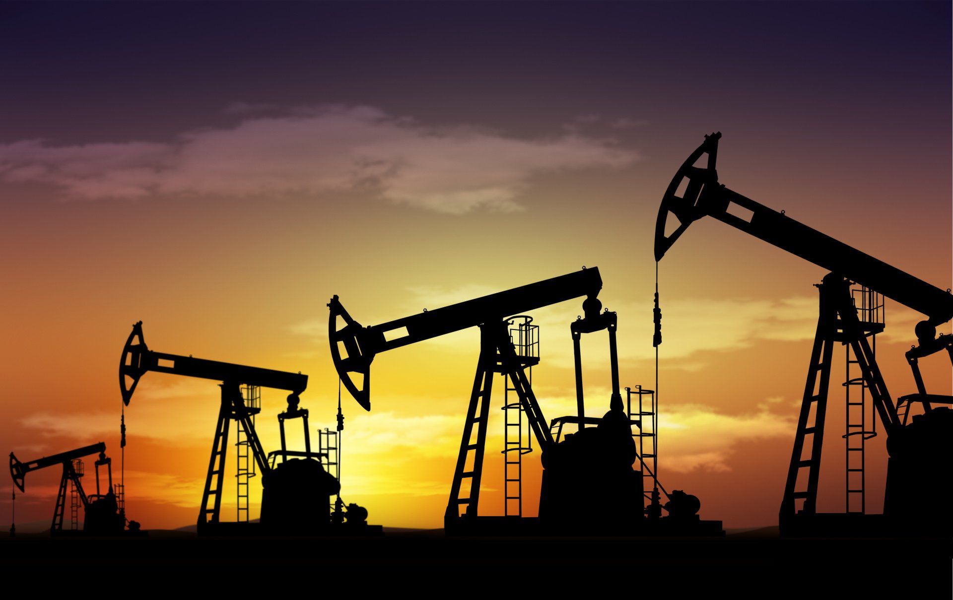 A row of oil pumps are silhouetted against a sunset sky