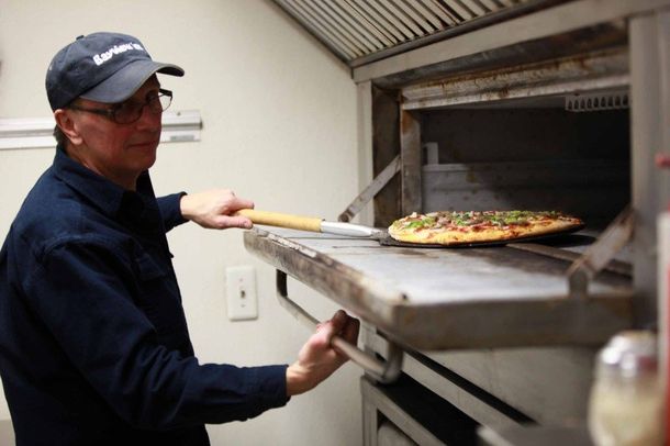 A man is taking a pizza out of an oven