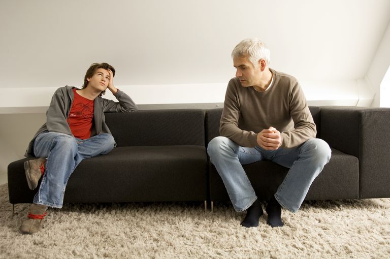 Two men are sitting on a couch talking to each other.