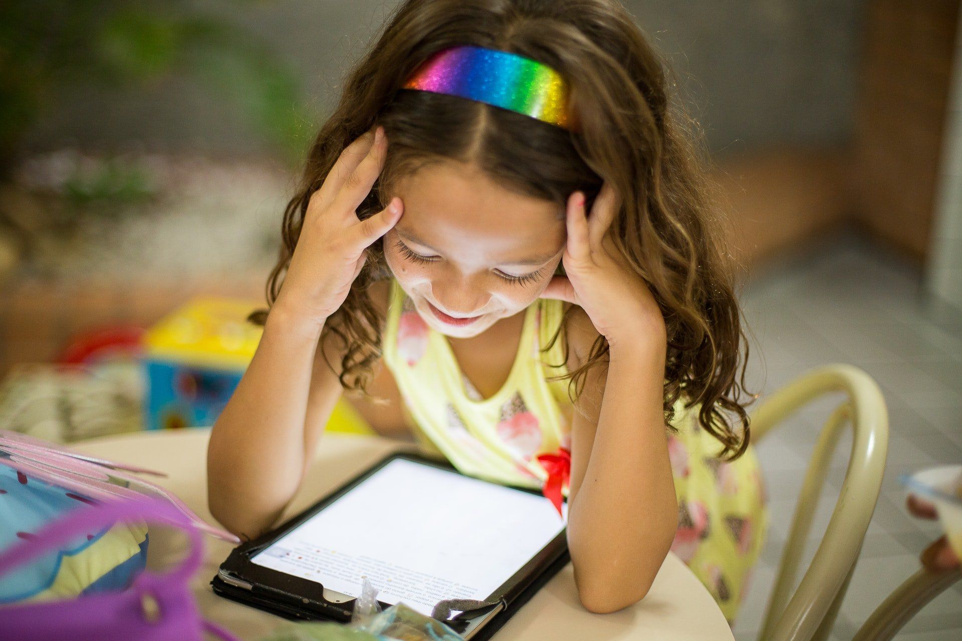A little girl is sitting at a table looking at a tablet.