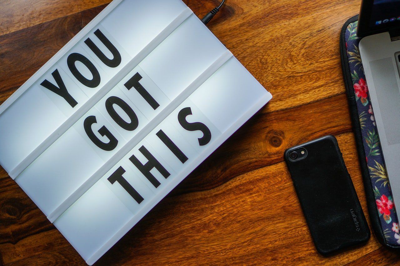 A sign that says `` you got this '' is on a wooden table next to a laptop and a cell phone.