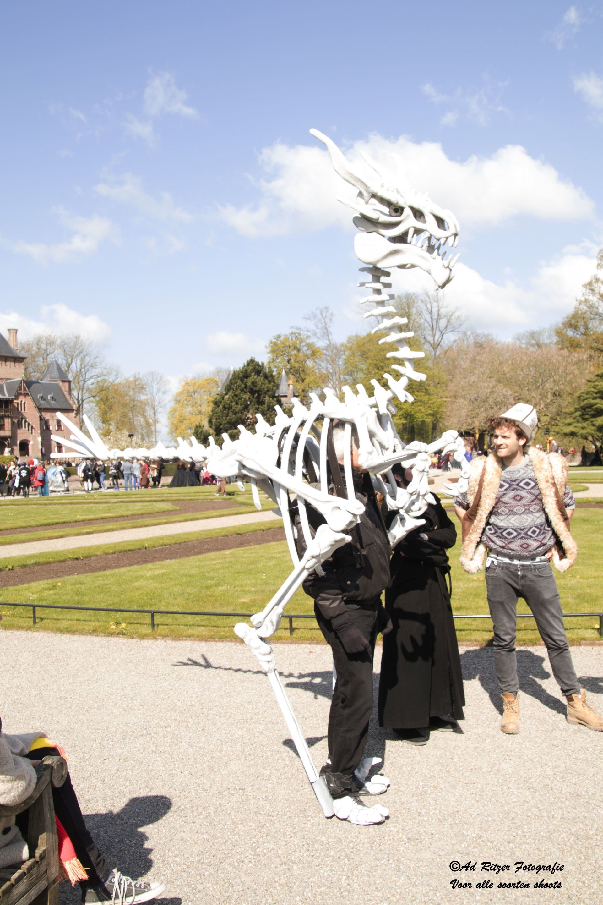 Persoon in een wit skeletkostuum poseert buiten op een zonnige dag in een park of op een festival.