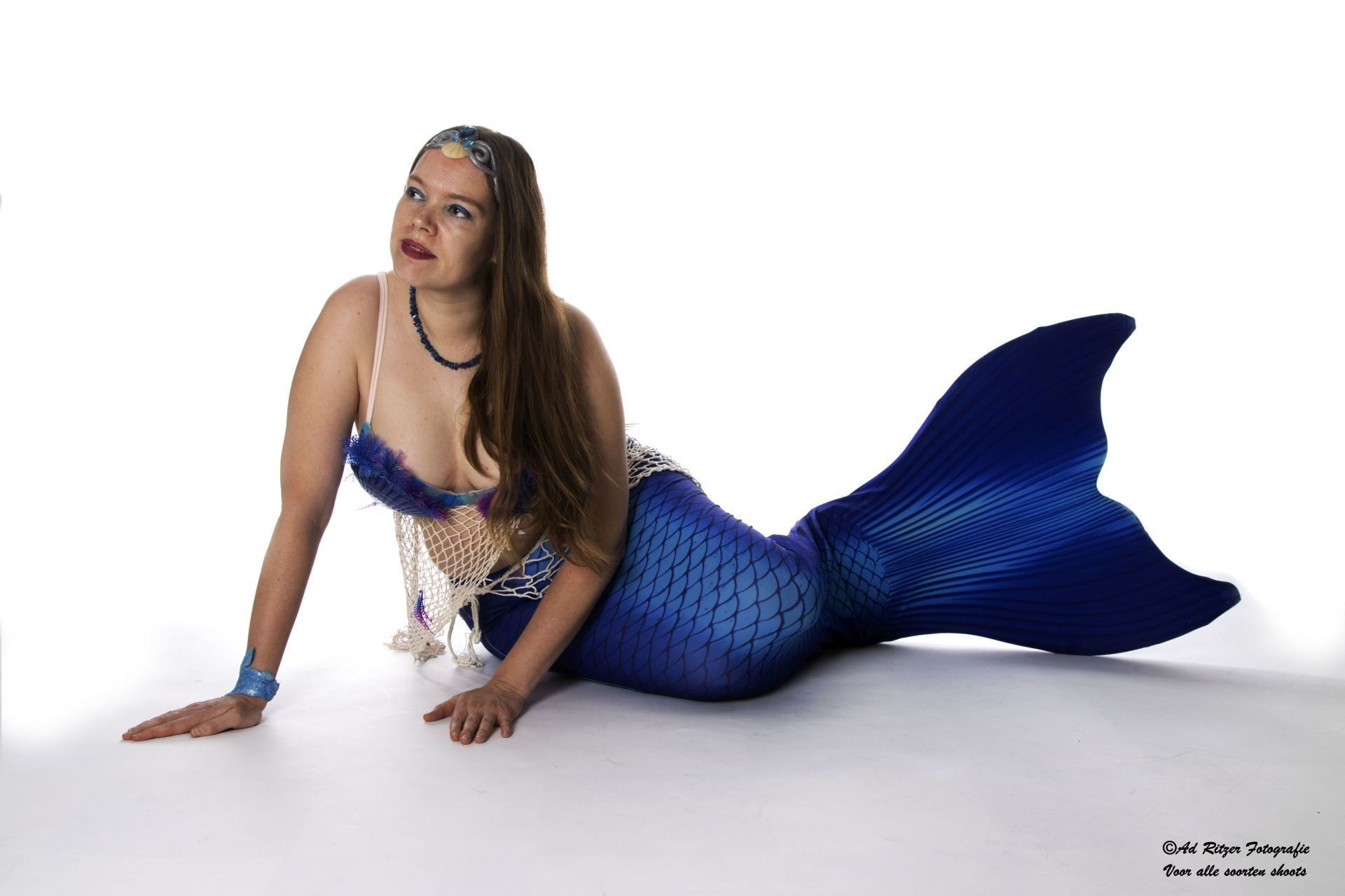 Vrouw poseert in een blauw zeemeerminnenkostuum tegen een witte achtergrond.