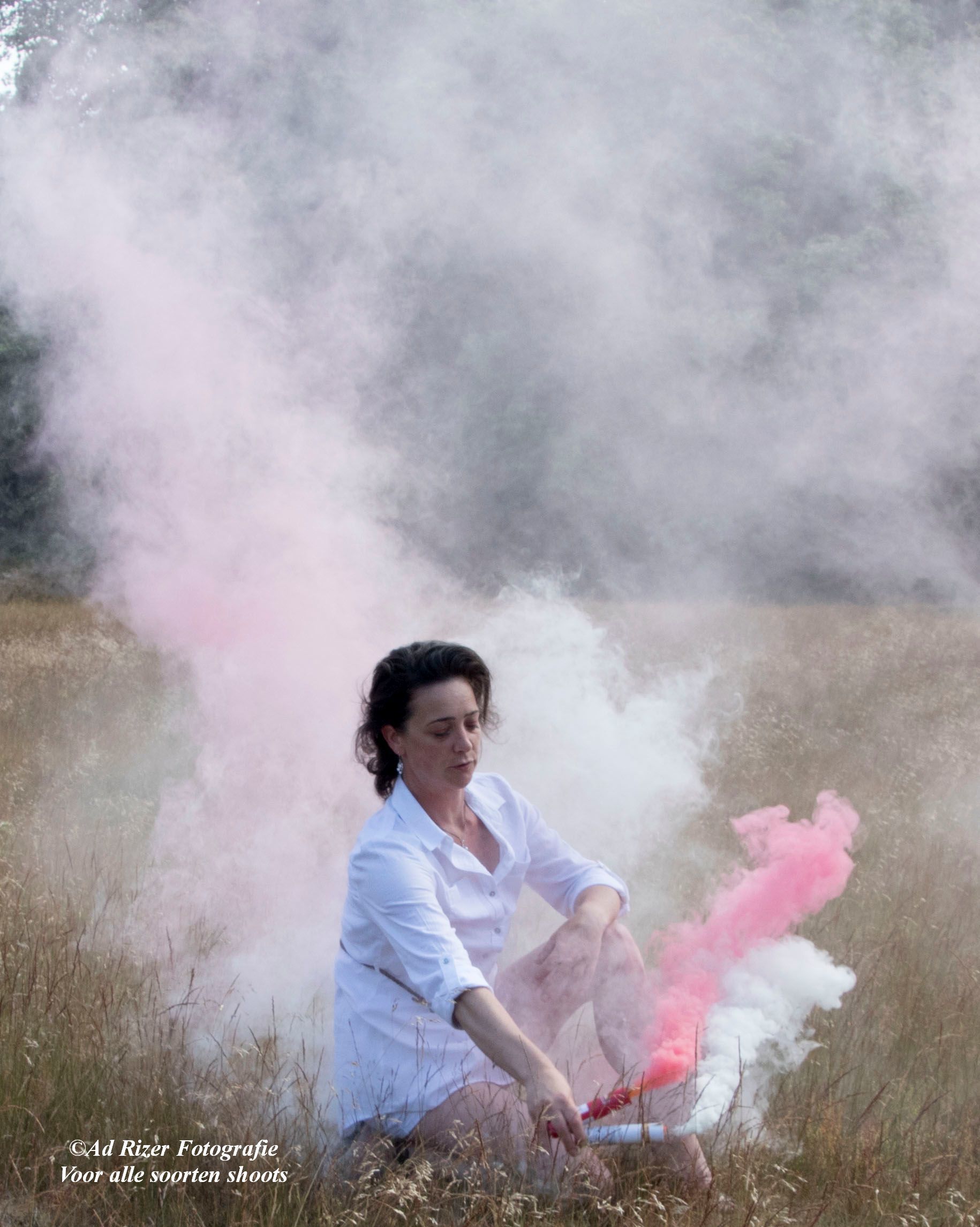 Een persoon knielt in een grasveld en laat roze rook vrijkomen uit een fakkel te midden van een wolk witte rook.