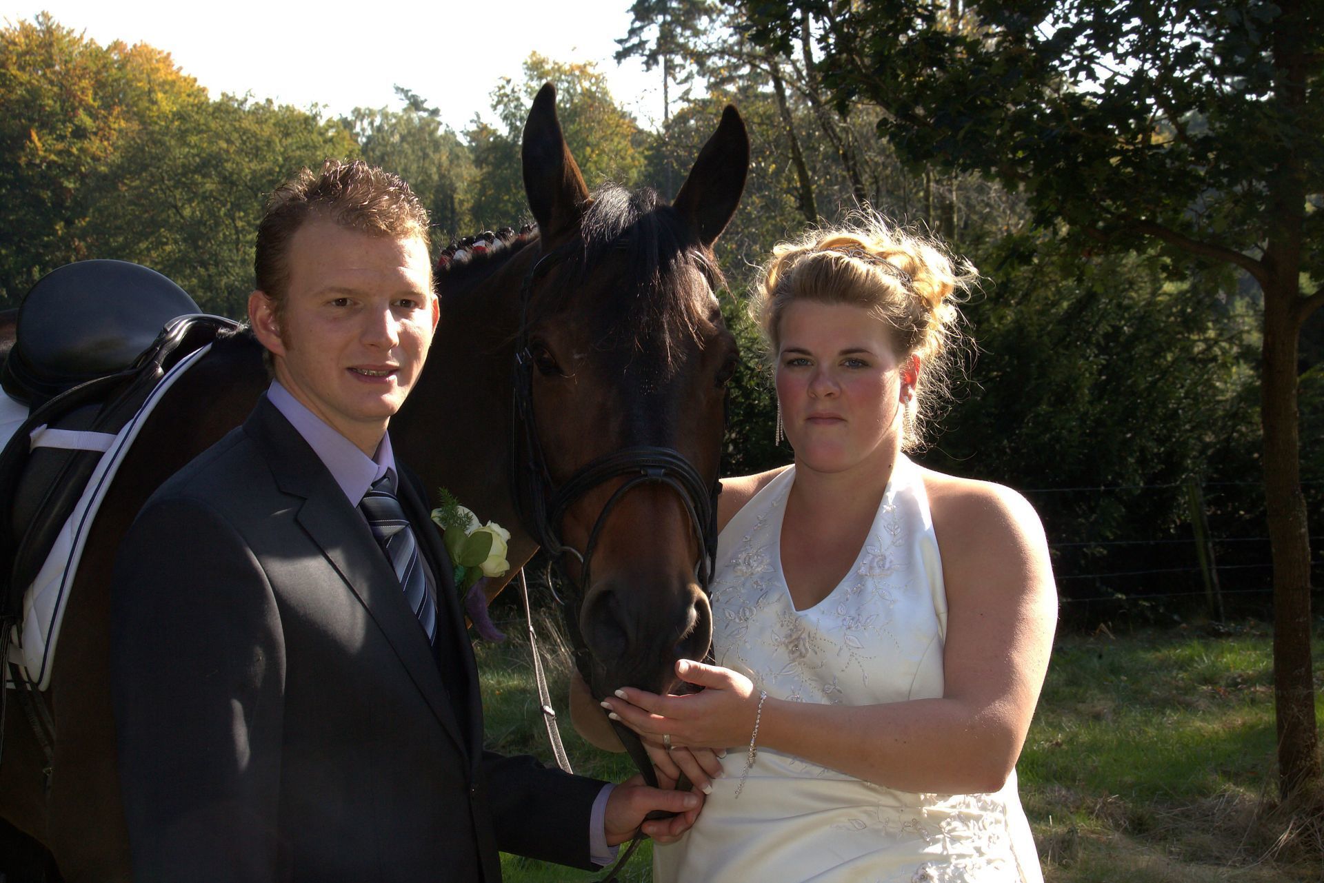 Een man en een vrouw in formele kleding staan ​​naast een paard in de zon.
