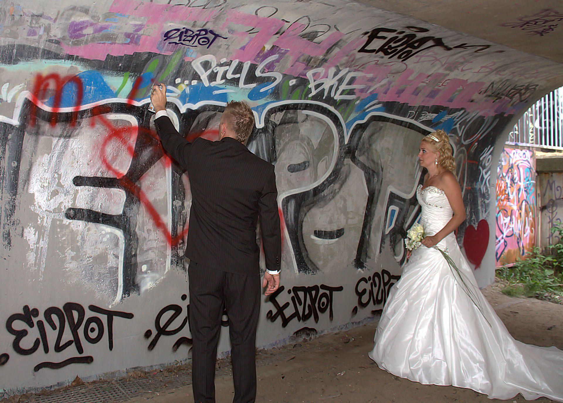 Een stel in galakleding onder een met graffiti bekladde tunnel, tegenover een muur en elkaar.