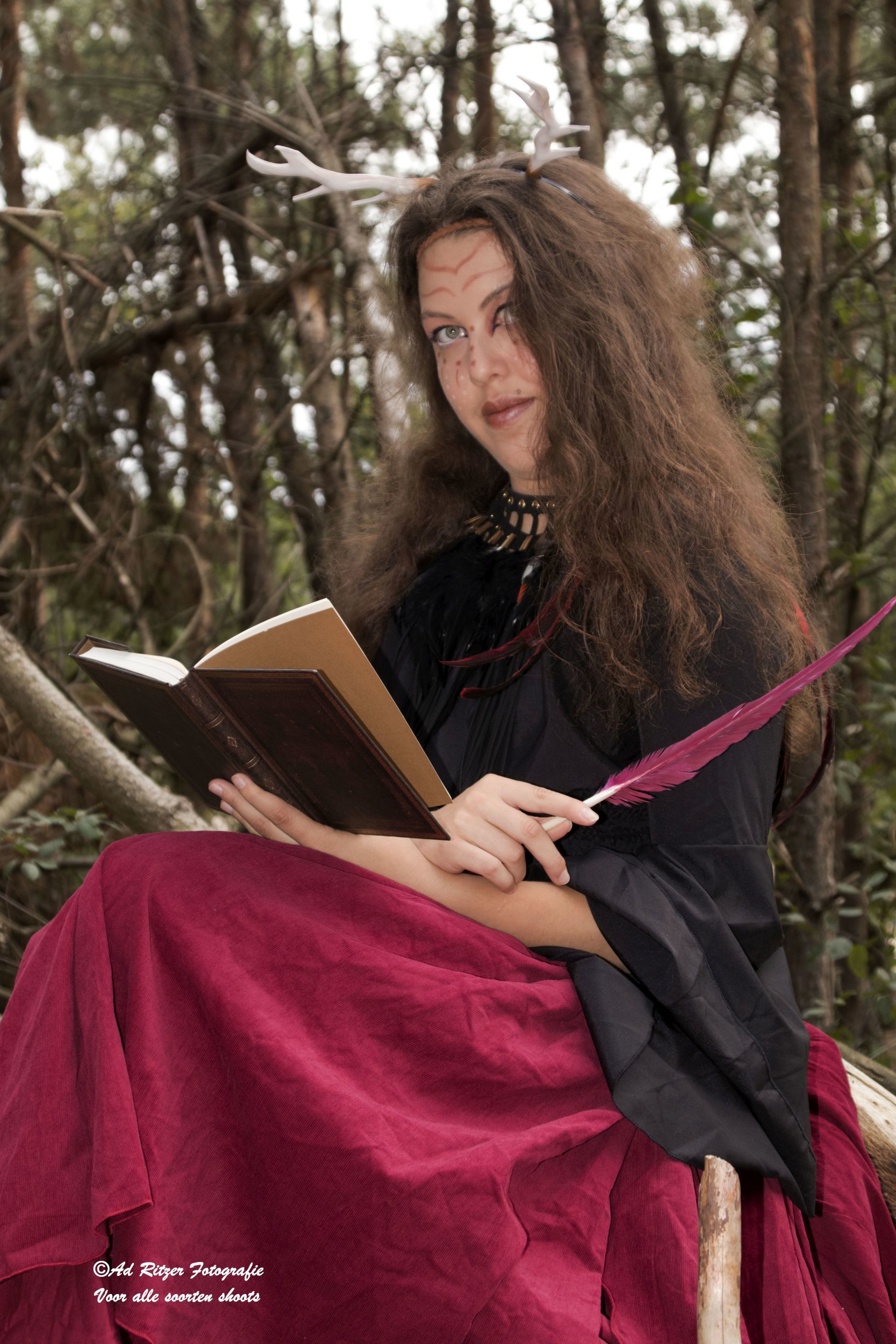 Vrouw in een zwarte mantel en magenta rok leest een boek in de buitenlucht tussen de bomen.