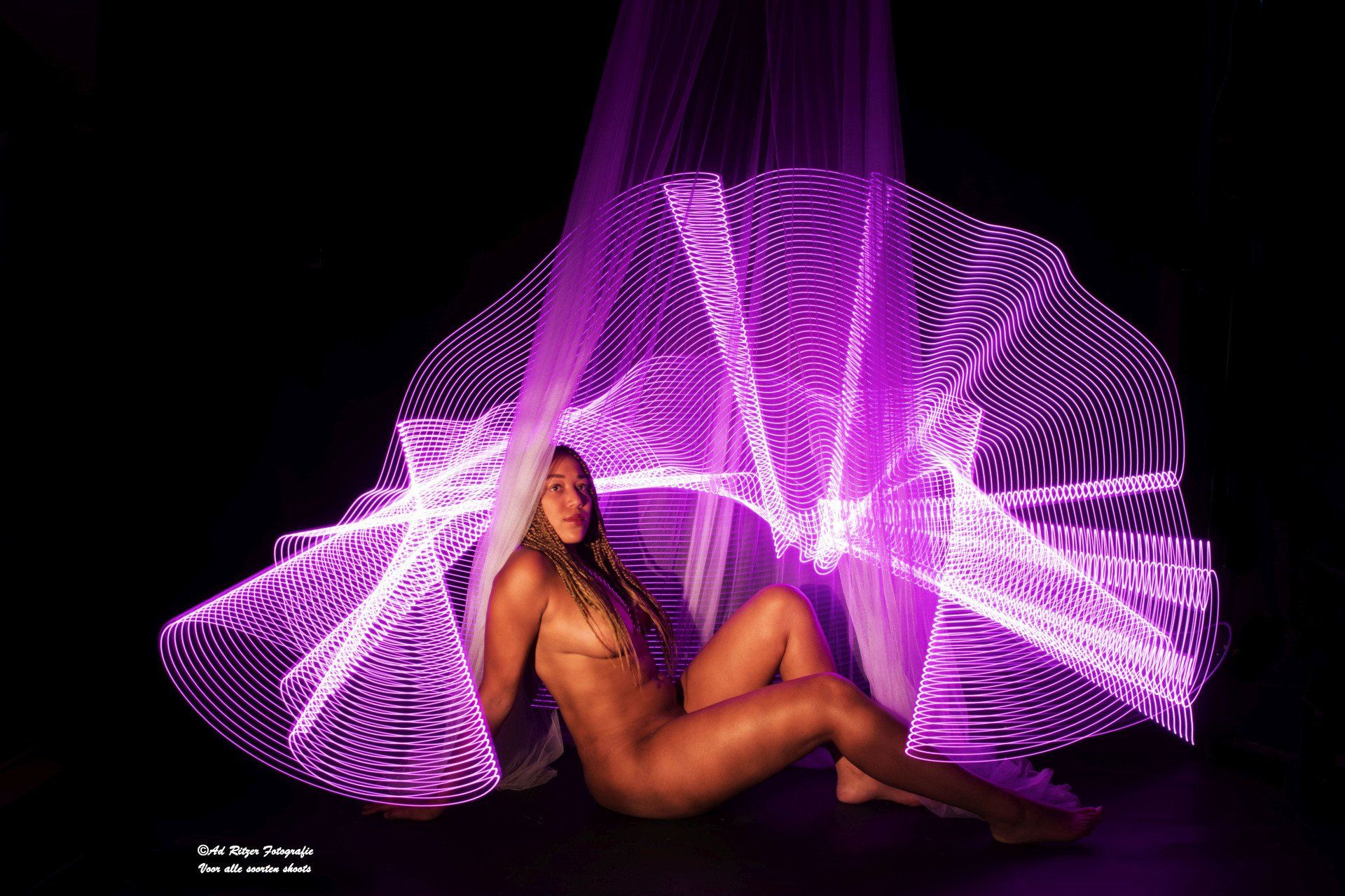 Vrouw poseert onder vloeiende paarse lichtsporen op een donkere achtergrond.