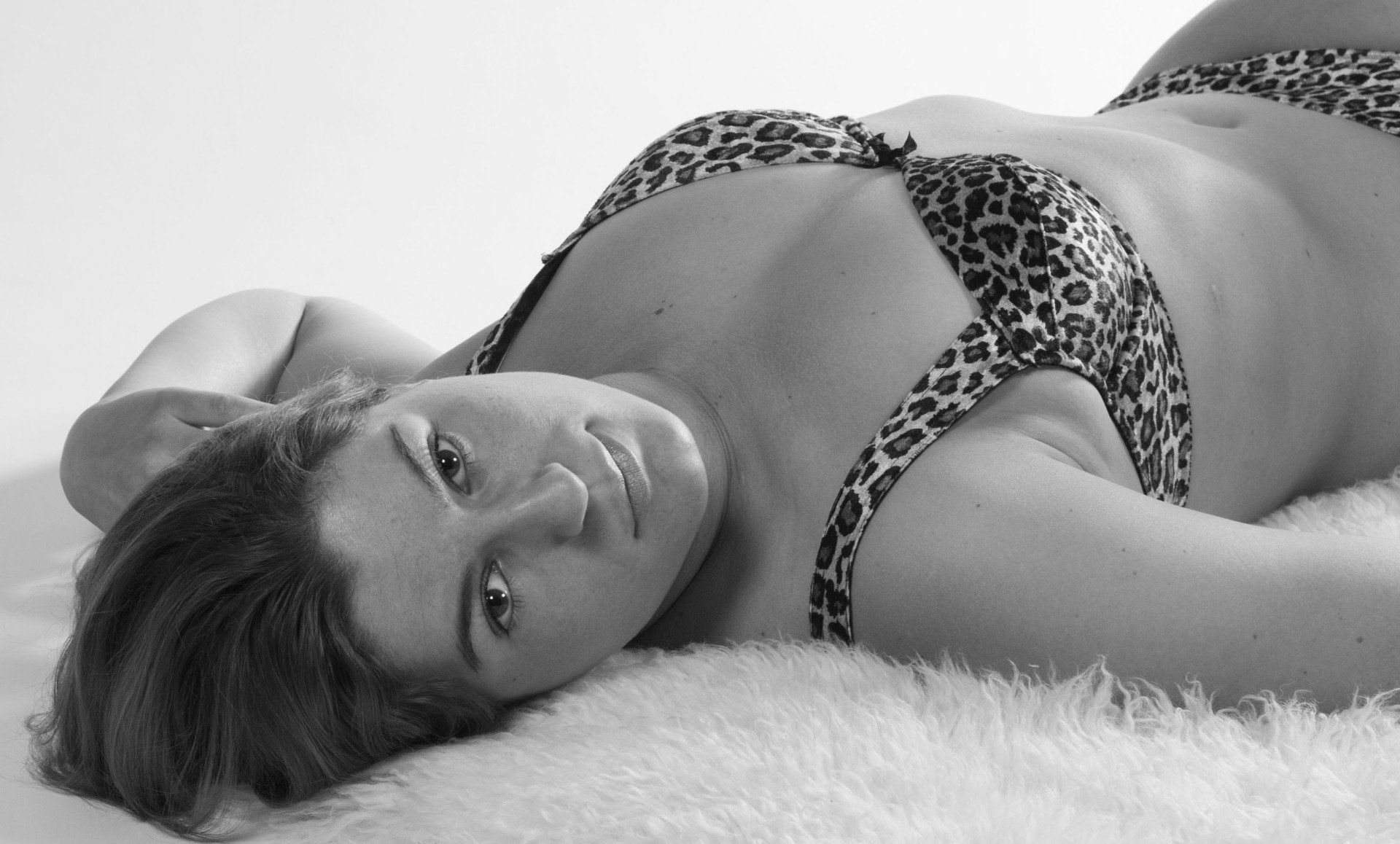 Vrouw ligt op een bed in lingerie met luipaardprint en kijkt naar de camera met haar hoofd op haar arm.